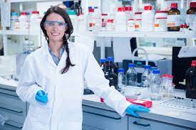 a scientist smiling Infront of a shelf full of chemicals 